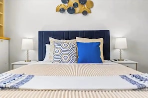 Cama bem arrumada com colcha estampada, dois travesseiros e um detalhe decorativo na parede acima.