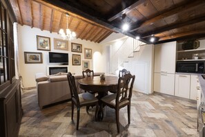 A dining area with a round table and chairs, a sofa, and a TV on the wall.