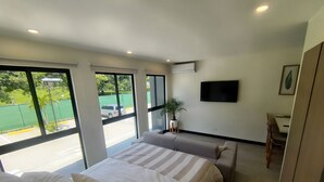 A modern hotel room with a large bed, a sofa, a TV, and a balcony with a view of the street and greenery. - Cosy Loft - 3 Minutes From Airport SJO (Alajuela)