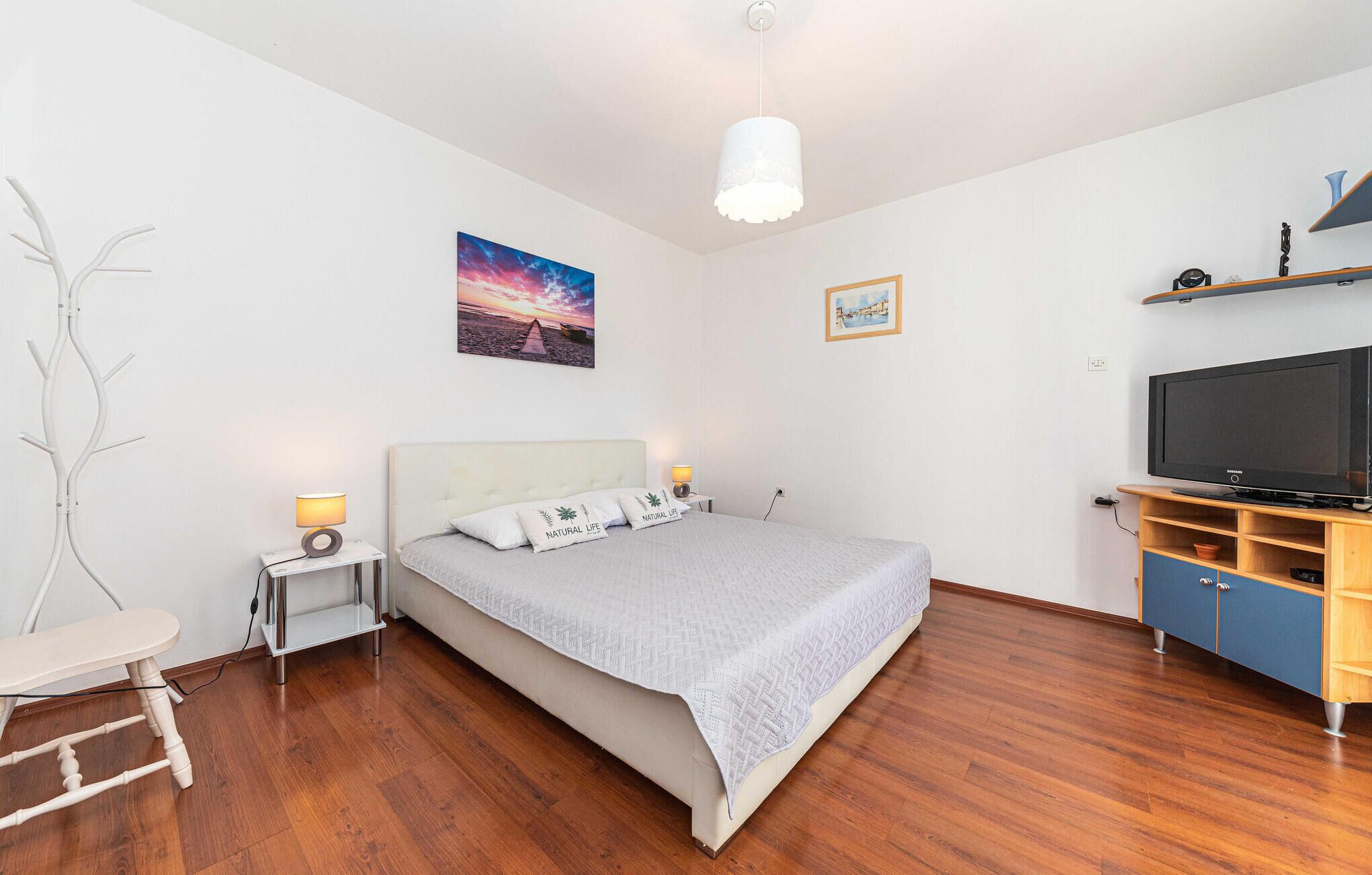 A bedroom with a bed, bedside tables, a TV, and a wooden floor.