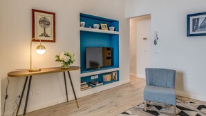 A living room with a TV on a blue shelf, a lamp, a chair, and a framed picture on the wall. - Apartments Florence - Borgo dei Greci (Firenze)
