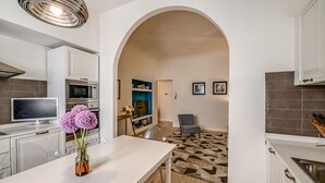 A modern kitchen with white cabinets, a built-in oven, and a dining area with a white table and chairs. - Apartments Florence - Borgo dei Greci (Firenze)