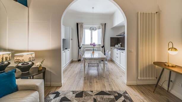 A modern kitchen with white cabinets, a dining table, and a central island. - Apartments Florence - Borgo dei Greci (Firenze)