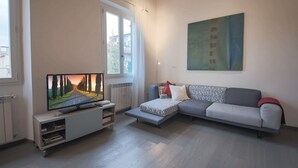 A modern living room with a flat-screen TV, a grey sofa, and a window with curtains. - Apartments Florence - Pepi Loft (Firenze)