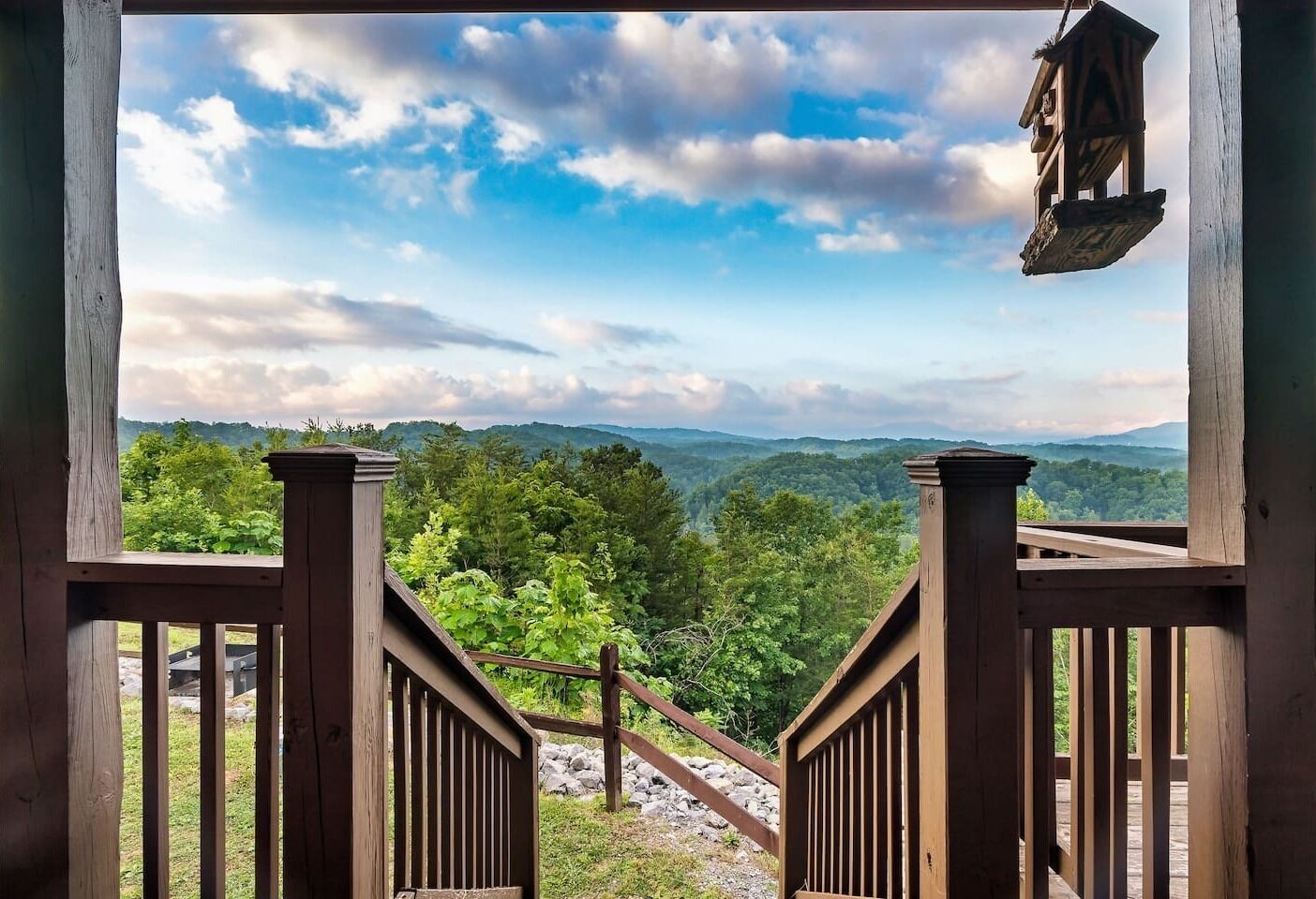 Un escalier en bois mène à un balcon d’où l’on peut admirer un paysage montagneux sous un ciel dégagé.