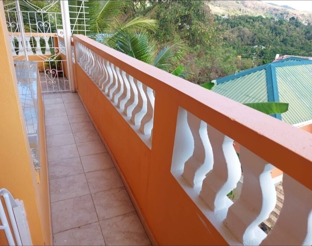 Un balcón con piso de baldosas y barandilla blanca decorativa.