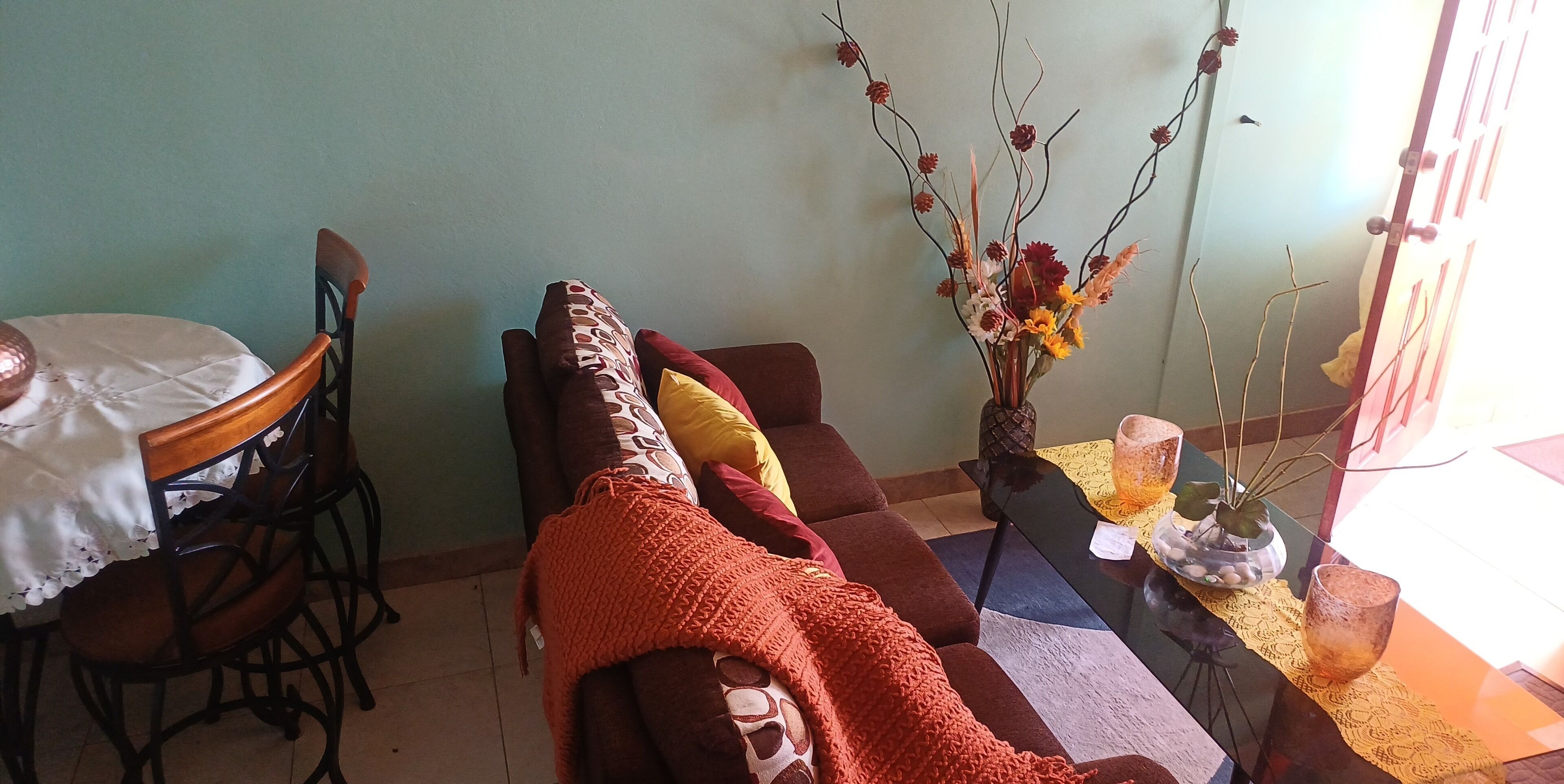 A living room with a sofa, a dining table with chairs, and a coffee table with a vase of flowers.
