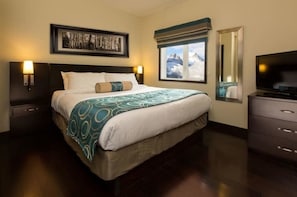 Relax in a spacious room with a large bed, flat-screen TV, and a dresser, offering a serene mountain view.