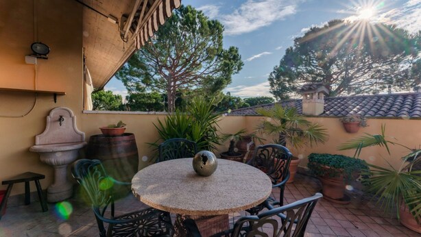 Une terrasse avec une table ronde, des chaises, des plantes en pot et une fontaine décorative en pierre.