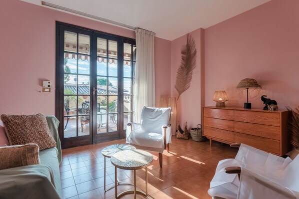 A room with a large sliding glass door leading to an outdoor area, a white chair, a wooden cabinet, and a small round table.