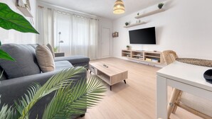 Moderni olohuone, jossa on sohva, sohvapöytä, televisio ja hyllyt.