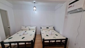 Une chambre avec deux lits simples, un plancher en bois, un luminaire au plafond et un appareil de climatisation.