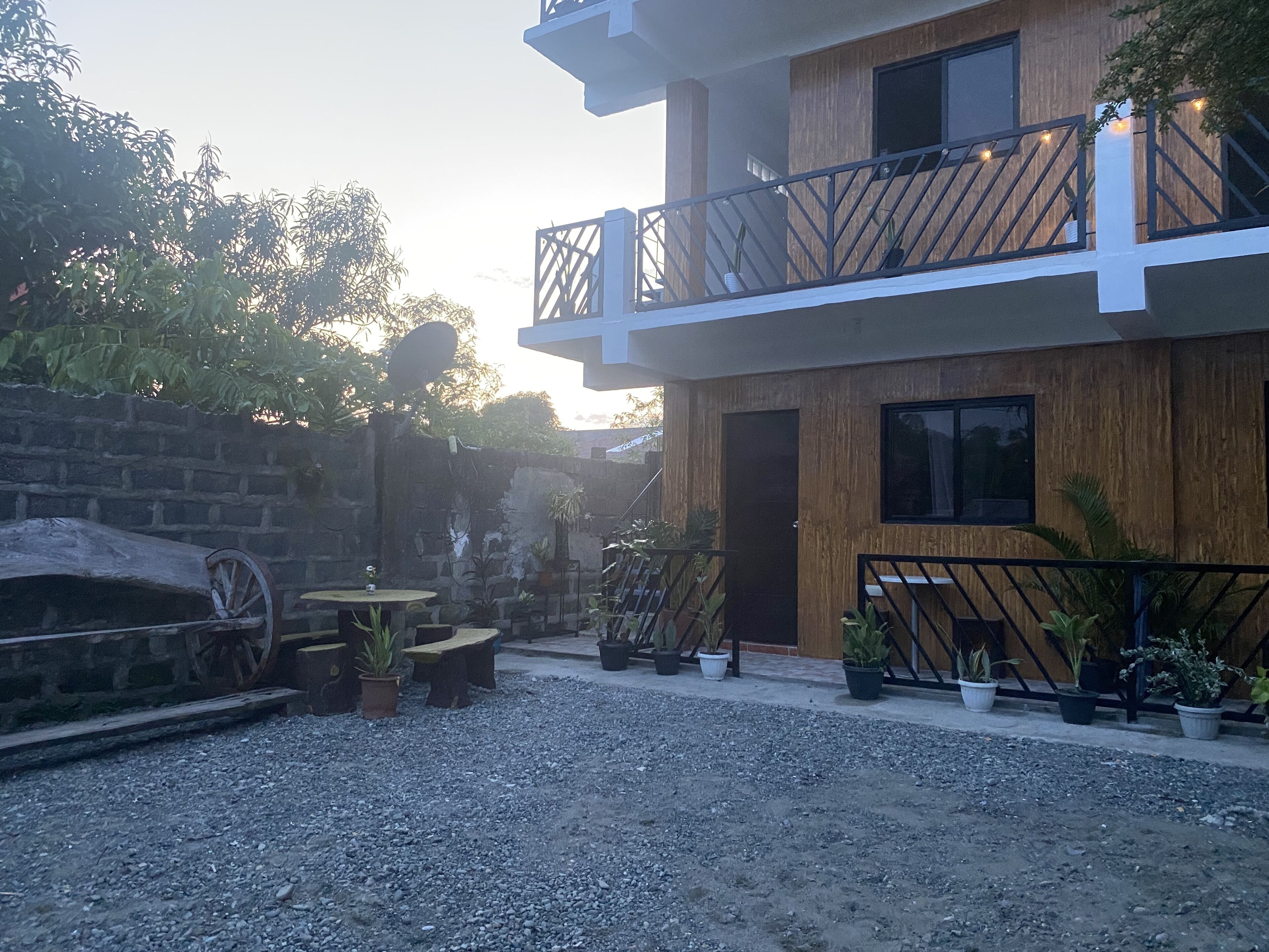 A modern two-story building with a balcony, potted plants, and a rustic stone wall.
