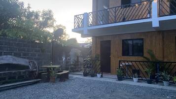 A modern two-story building with a balcony, potted plants, and a rustic stone wall.