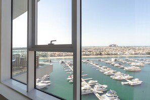 A marina with numerous boats docked, a clear sky, and a distant cityscape.