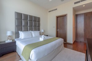 A hotel room with a large bed, a grey headboard, two bedside tables with lamps, a wooden wardrobe, and a door.