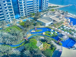 A high-rise hotel with multiple balconies, a pool area with lounge chairs and umbrellas, and a beach view. - Modern, Charming, Sea View Apt. In Palm Jumeirah (Dubai)