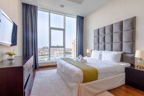 A hotel room with a large bed, a view of the city, a flat-screen TV, and a desk with a vase of flowers.