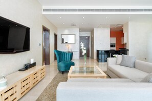 A modern living room with a flat-screen TV, teal armchair, and a beige sofa.