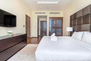 A hotel room with a large bed, a flat-screen TV mounted on the wall, a wooden dresser, and a door leading to another room.