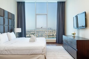 A hotel room with a large bed, a flat-screen TV, a dresser, and a city view through the window.