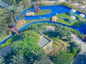 An aerial view of a resort with a large swimming pool, palm trees, and sun loungers.
