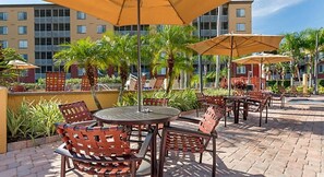 Relax on the patio surrounded by lush greenery and tropical plants, with comfortable seating and umbrellas for shade.