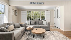 Un salon avec un canapé gris, une table basse ronde et une grande fenêtre avec des volets.