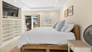 Une chambre avec un lit, un téléviseur fixé au mur, un ventilateur et une porte coulissante donnant sur un espace extérieur.