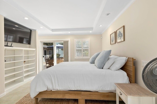 Quarto com cama, TV fixada na parede, ventilador e porta deslizante para área externa.