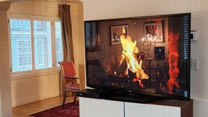 A modern living room with a flat-screen TV on a white entertainment unit, a grey sofa, and a red patterned rug.