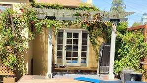 A covered patio with a wooden deck, a white outdoor sofa, and a pergola with climbing plants.