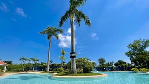 Une piscine d’eau cristalline, entourée de palmiers, avec un panneau indiquant « Interdiction de plonger ».