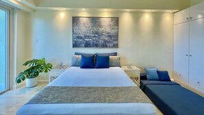 Une chambre à coucher moderne avec un grand lit, des tables de chevet, une petite table, une plante en pot et une armoire.