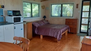 A compact room with a bed, a small desk, a kitchenette, and a window with blinds. - Te Oneroa Hill, 5 acres of native park with wonderful sea view. (Russell)