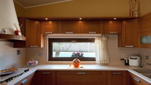 A modern kitchen with wooden cabinets, a window with a view of a pool, and a small orange toy on the counter. - Villa in Melissano with 4 bedrooms sleeps 8 (Melissano)