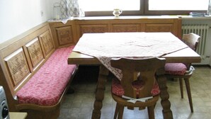 Una cucina con una panca di legno, un tavolo con una tovaglia di pizzo e una finestra con una tenda.