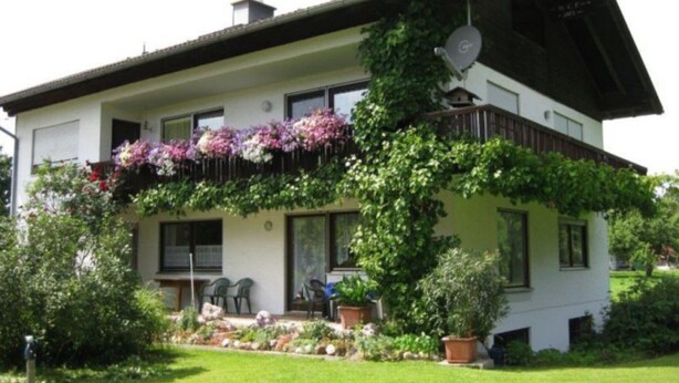 Una casa a due piani con un balcone fiorito, un'antenna parabolica e un giardino curato.