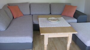 Un divano angolare grigio con cuscini arancioni, un tavolino in legno con un sottopiattino bianco e una ciotola bianca sul sottopiattino.