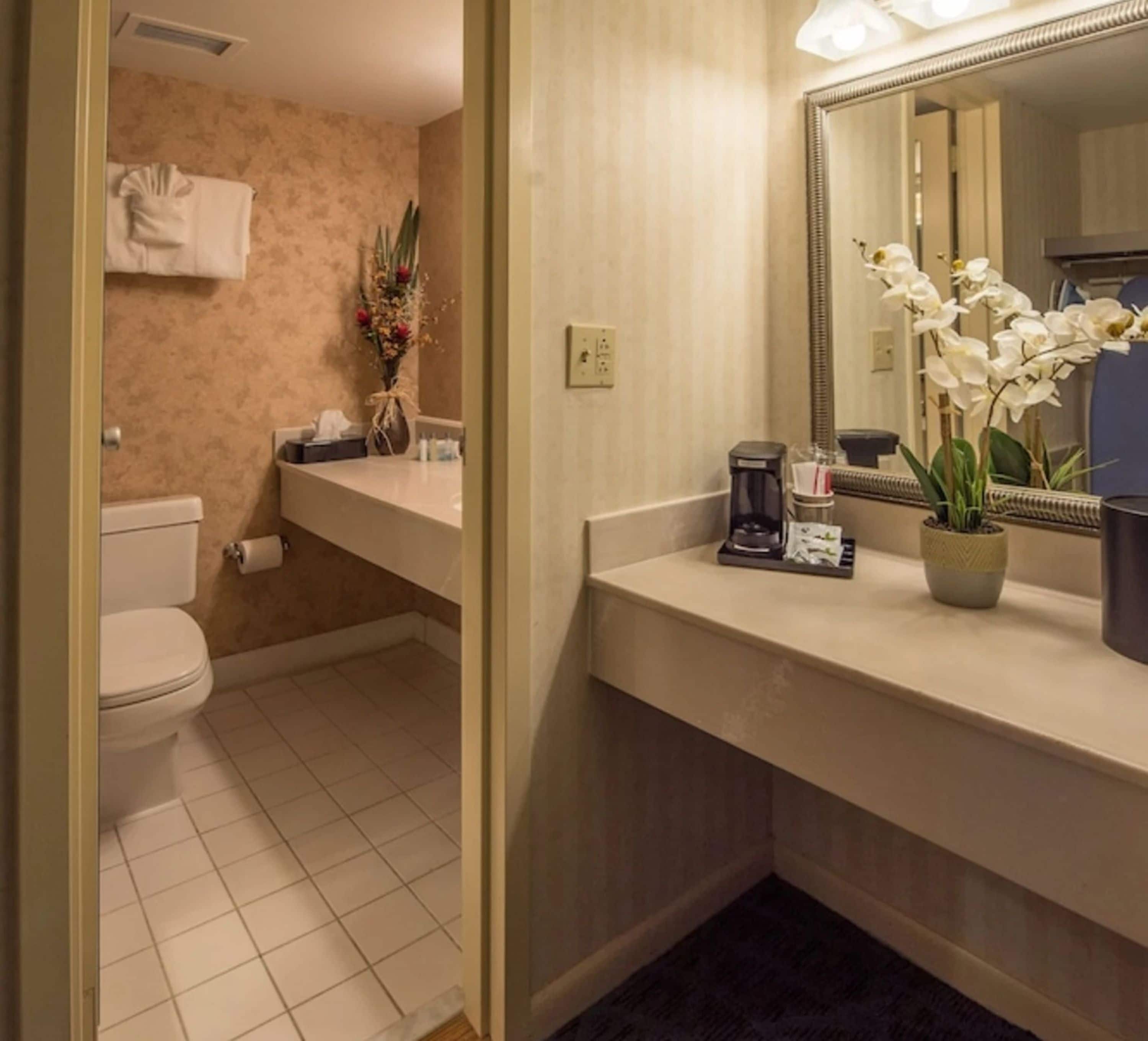 A bathroom with a toilet, sink, and mirror. There is a vase with flowers on the sink counter.