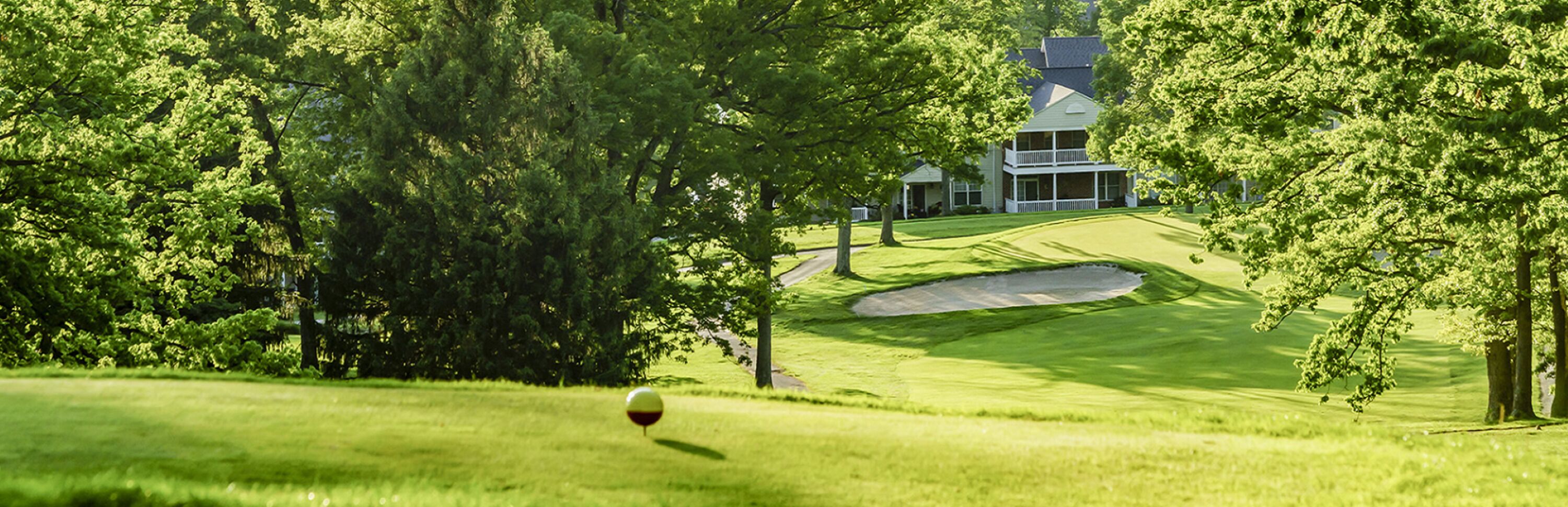 A golf course with a sand bunker and a house in the background.