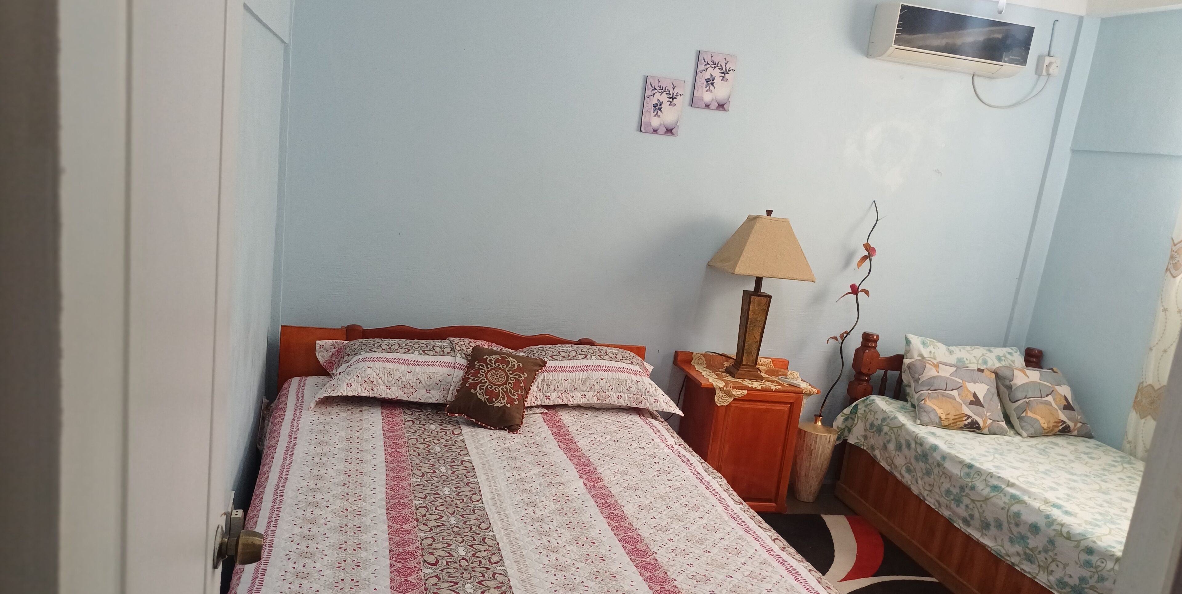 Ein Schlafzimmer mit zwei Betten, einem Nachttisch mit Lampe, einem an der Wand befestigten Fernseher und zwei Wandbildern.