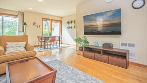 A living room with a sofa, a dining area with chairs, a painting of a sunset, and a clock on the wall. - 3BR & 2.5BA centrally located home with AC, 2 Masters, 4 Smart TVs & Fiber Wifi! (Seattle)
