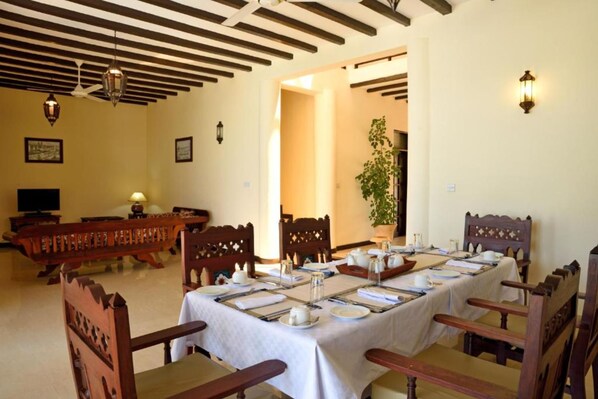 A dining area with a long table set for a meal, wooden chairs, and a ceiling with exposed beams. - Villa Serenity Zanzibar (Paje)