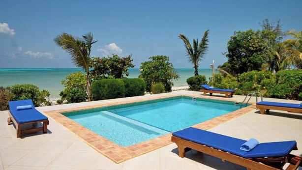A pool with blue lounge chairs and a view of the ocean. - Villa Serenity Zanzibar (Paje)