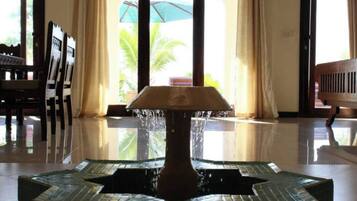 A lobby with a tiled fountain, a wooden bench, and a view of palm trees through the glass doors.