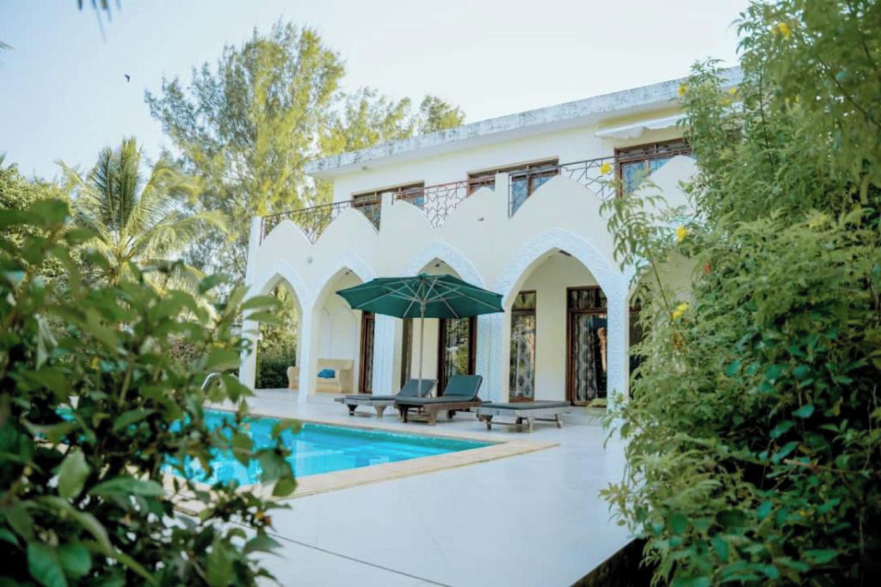A poolside area with a white building, green umbrellas, and lounge chairs.