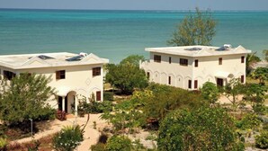 Two white buildings with solar panels, surrounded by greenery and overlooking a turquoise sea. - Villa Serenity Zanzibar (Paje)