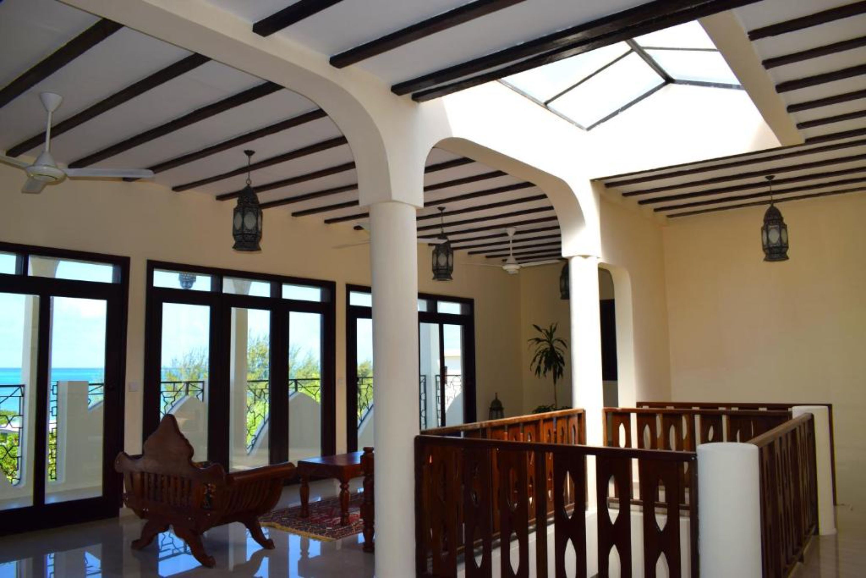 A spacious indoor area with large windows, wooden beams, and a balcony with a view.