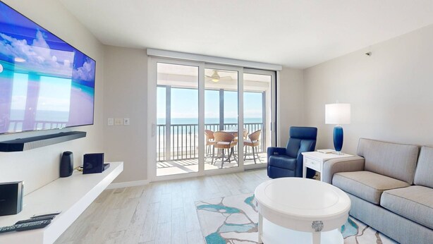 A hotel room with a balcony, a television, a sofa, a coffee table, and a lamp.